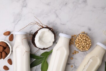 Different types of vegan milk in bottles with ingredients and leaves on white marble table, flat lay