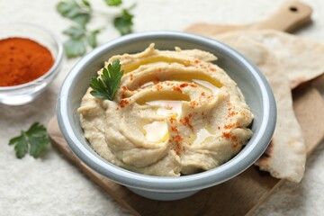 Delicious hummus with olive oil, parsley and paprika in bowl on white table, closeup