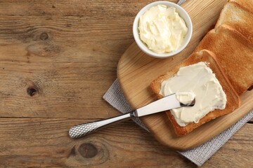 Delicious toasted bread slices with butter and knife on wooden table, flat lay. Space for text