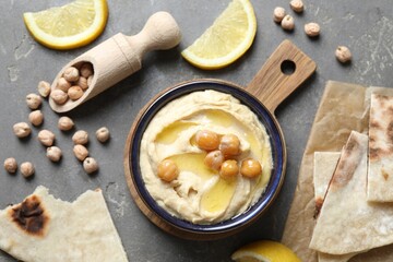 Delicious hummus with olive oil, chickpeas, lemon and pita on grey textured table, flat lay