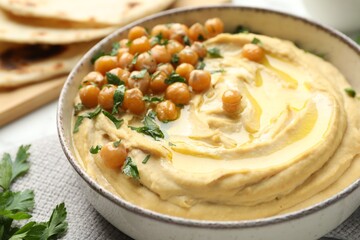 Delicious hummus with olive oil, chickpeas and parsley in bowl on table, closeup