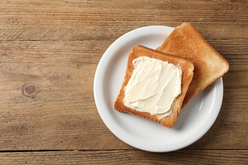 Delicious toasted bread slices with butter on wooden table, top view. Space for text