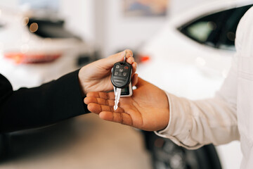 Detail cropped shot of unrecognizable black male buyer getting car key and greetings from auto dealer while buying new auto in dealership. African car owner during handing over keys at auto showroom