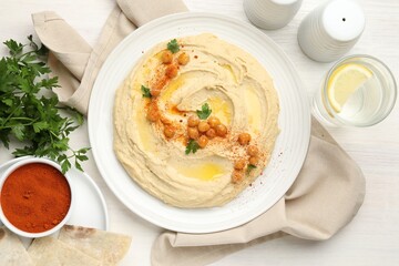 Delicious hummus with olive oil, chickpeas and paprika served on white wooden table, flat lay