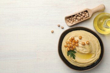 Delicious hummus with olive oil, chickpeas and parsley on white wooden table, flat lay. Space for text