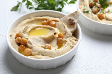 Delicious hummus with olive oil, chickpeas and pita in bowl on light textured table