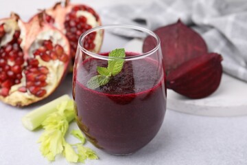 Tasty beetroot smoothie with mint in glass, fresh vegetables and pomegranate on light table, closeup. Vegan drink