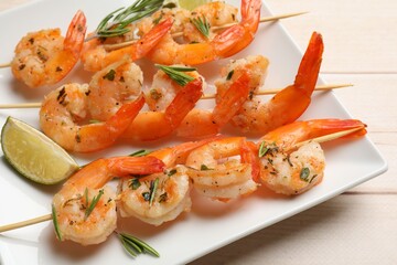 Skewers with delicious grilled shrimps and lime on wooden table, closeup