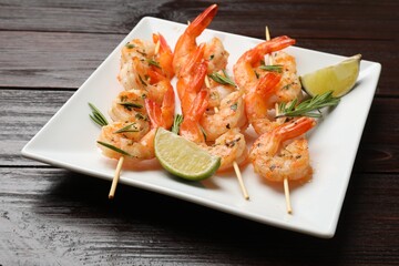 Skewers with delicious grilled shrimps and lime on wooden table