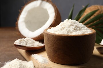 Coconut flour in bowl, spoon and fresh fruits on wooden table, closeup