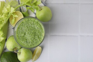 Tasty green smoothie in glass, lime, celery and apples on white tiled table, flat lay. Space for text