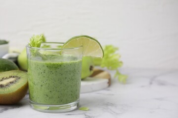 Tasty green smoothie in glass with lime and products on white marble table, closeup. Space for text