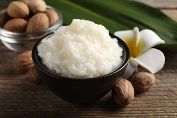 Natural shea butter in bowl, nuts and plumeria flower on wooden table, closeup