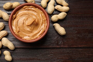 Tasty peanut butter in bowl and nuts on wooden table, flat lay. Space for text