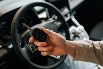 Closeup cropped shot of young man sitting in drivers seat behind steering wheel in car. Close-up of happy unrecognizable driver male holding key to new car in hand. Concept of smart key car technology