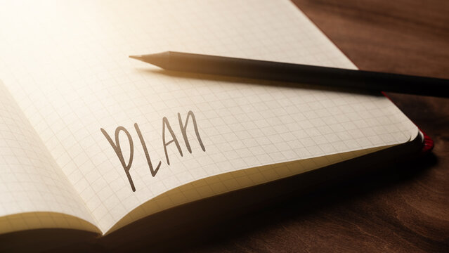 A handwritten inscription "Plan" on a grille of an open notebook on a wooden countertop, next to a black pencil, lighting of light. (selective focus), translation: plan