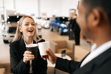 Closeup of cheerful multi-ethnic business people in formal outfit having break after meeting, talking during drinking coffee together in auto dealership. Concept lifestyle of businesspeople.