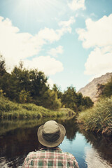 Landscape, water and person with rowing in lake for camping adventure, scenery and exploring nature with blue sky. Kayak, tourist and back in river for canoeing, summer holiday and fun hobby with hat