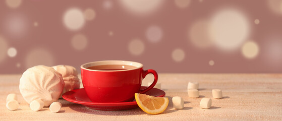 Red cup with hot brewed tea, slices of lemon and marshmallow on white wooden table against blurred background