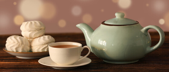 Teapot, zephyr and cup with hot brewed tea on wooden table against blurred background