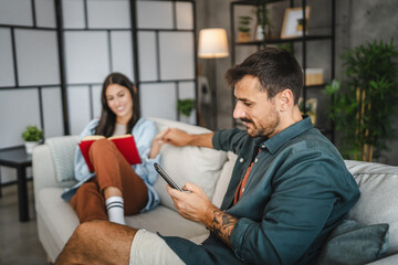 relaxed couple girlfriend read a book and boyfriend use mobile phone