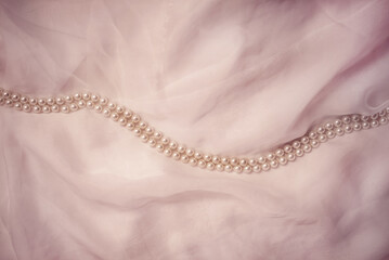A necklace of pearls lies on a white cloth
