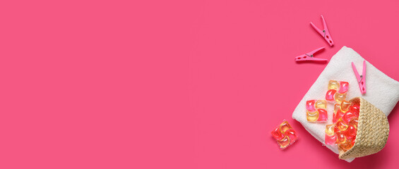 Gel capsules with laundry detergent, clean towel and clothespins on pink background