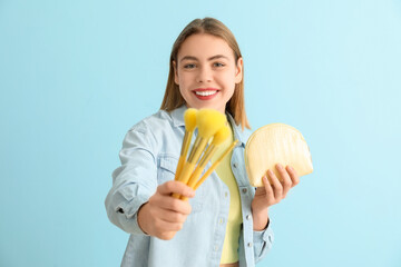 Young woman with cosmetic bag and makeup brushes on blue background