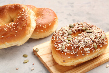 Wooden board of tasty bagels with sesame and pumpkin seeds on grunge background, closeup