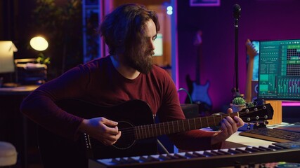 Portrait of male songwriter playing acoustic guitar and recording musical sounds to use for mix and...