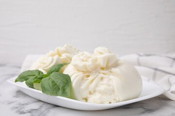 Delicious burrata cheese and basil on white marble table, closeup