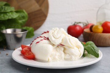 Delicious fresh burrata cheese with basil leaves and tomato on grey table