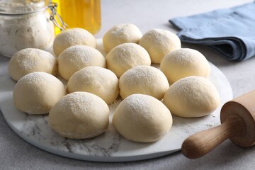 Raw dough balls, flour and rolling pin on light grey table