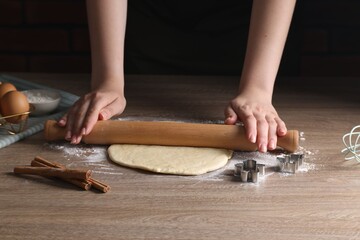 Woman rolling out dough for cookies at wooden table, closeup