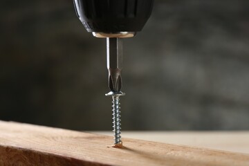 Screwing screw into wooden plank against gray background, closeup