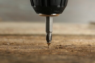 Screwing screw into wooden surface, closeup view