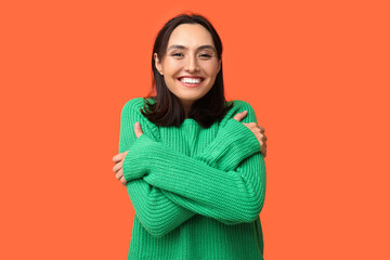 Fototapeta premium Young woman hugging herself on orange background