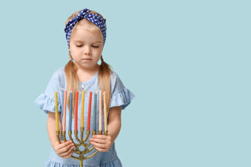 Cute little girl with menorah on blue background. Hanukkah celebration