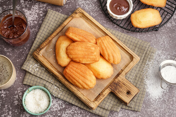 Wooden board with tasty madeleines on bowl with coconut flakes on grey background