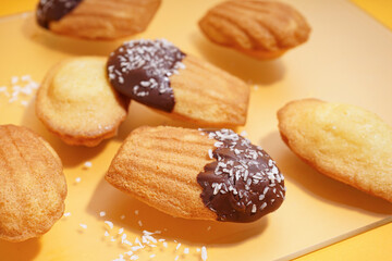 Delicious madeleines with chocolate and coconut flakes on yellow background