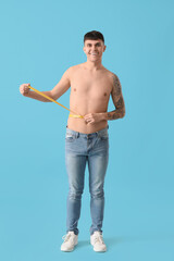 Fototapeta premium Young man with measuring tape on blue background. Diet concept