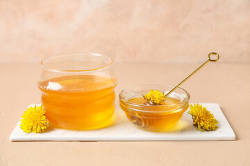 Bowl and glass of sweet honey with dipper on beige table