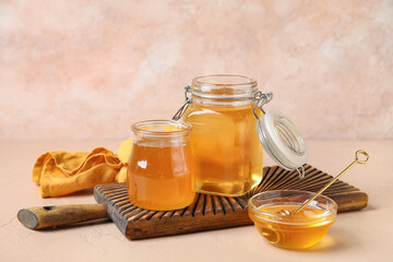 Jars and bowl of sweet honey with dipper on beige table