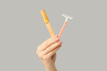 Female hands holding razor and spatula with sugaring paste on grey background