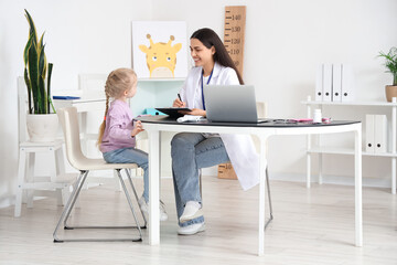 Female pediatrician working with little girl at table in clinic