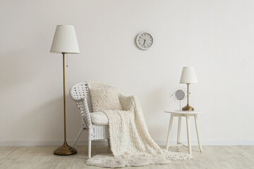Stylish living room with armchair, lamp and clock on white wall