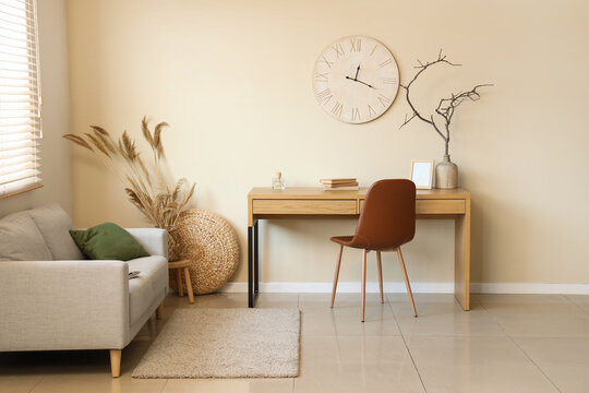 Stylish living room with sofa, workplace and clock on beige wall