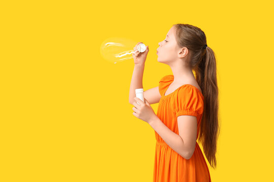 Cute girl blowing soap bubbles on yellow background