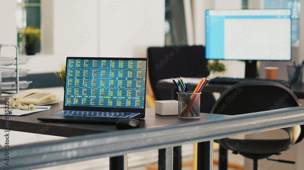 Poster office with laptop showing stock market listings and display in background with scheduled clients li