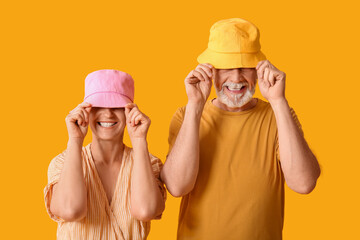 Mature couple in bucket hats on yellow background